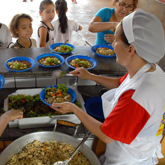 Foto de mulher servindo merenda as crianças em uma escola