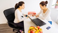 Consulta de paciente mulher com nutricionista mulher. Computador sobre a mesa, frutas, fita métrica e arquivos.