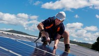 Profissional homem instalando placas de energia solar, céu azul com nuvens no fundo.